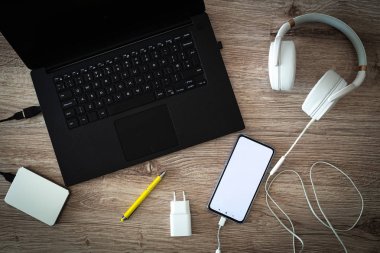 Bağlı kulaklıklı taşınabilir diske ve masanın üzerinde akıllı telefona sahip dizüstü bilgisayar. Dinlenme yeri veya iş yeri. Yazıt yeri olan beyaz telefon ekranı
