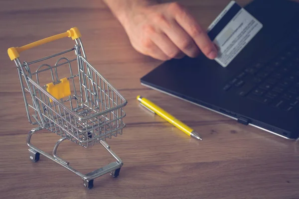 İnternet alışverişi. Laptop, banka kartı ve bir bardak çayla alışveriş arabasının küçük resmi. Kavram. Evden çıkmadan alışveriş yapmak daha uygun olur.