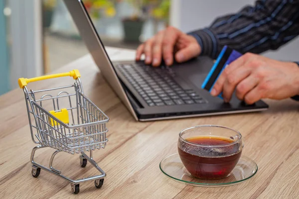 Internet shopping.  Thumbnail of a shopping trolley with laptop, bank card and glass of tea.  Concept.  Convenient shopping without leaving your home