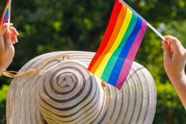 LGBT bayrakları sallayan şık yaz şapkalı bir kadın.