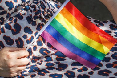 LGBT gökkuşağı bayrağını kucağında tutan benekli elbiseli bir kadın.