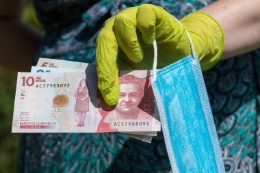 Lastik eldivenli bir kadın elinde Kolombiya pezosu ve antivirüs maskesi tutuyor.