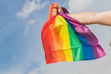 Adam elinde sıkıca tutarak LGBT hareketinin gökkuşağı bayrağını tutuyor. Eşitlik savaşında bir güç ve kararlılık ifadesi.