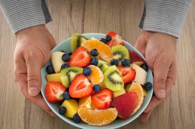 Erkeklerin elleri gömleğin içine çeşitli meyve çeşitleriyle dolu dekoratif bir tabak koydu. Sağlıklı ve ferahlatıcı bir salata.