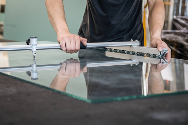 Квалифицированный работник режет бесцветное стекло на профессиональном столе специальными инструментами