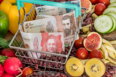 Yiyecek ürünleri, sebzeler ve meyvelerin etrafında Kolombiya pezosu olan bir alışveriş sepeti. Enflasyon, yükselen fiyatlar ve daha pahalı gıda kavramı