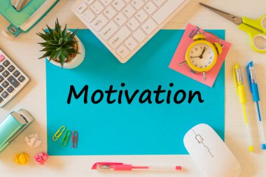 Masanın üzerinde motivasyon sözcüğünün yazılı olduğu büyük bir mavi kart. Ofis ve okul aksesuarları, bilgisayar klavyesi, hesap makinesi, kalemler, buruşmuş kağıt topları, makas, tencerede küçük bir çiçek, zımbalar. Geliştirme işi konsepti
