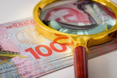 Üstünde büyüteç olan bir tomar Yeni Zelanda 100 dolarlık banknot. Bankacılık ve yatırım kavramı