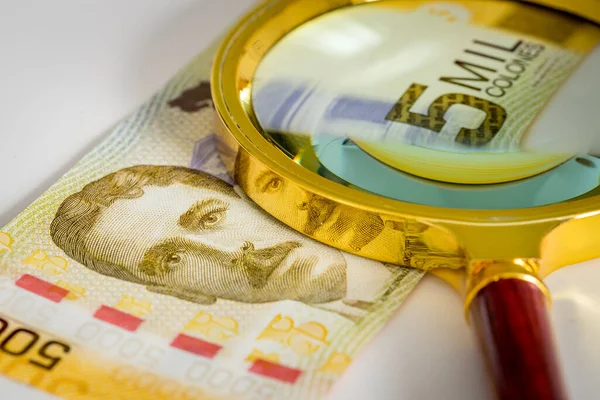 Kosta Rika parası. Üzerinde büyüteç bulunan beş bin Colone banknotu. İş ve bütçe kavramı
