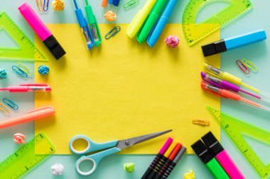 okul ve ofis eşyaları, renkli kalemler, zımbalar, işaretleyiciler, set kareleri, ortada boş sarı bir metin sayfası.