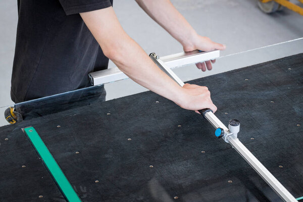 Мужчина режет стекло с помощью специальных инструментов в стеклянной мастерской