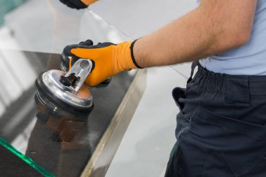 Glazier pencereler için bir enayi kullanıyor. Cam yapım atölyesi, adam özel aletlerin yardımıyla masanın üzerindeki kalın cam levhayı kaldırır.