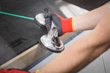 Glazier pencereler için bir enayi kullanıyor. Cam yapım atölyesi, adam özel aletlerin yardımıyla masanın üzerindeki kalın cam levhayı kaldırır.