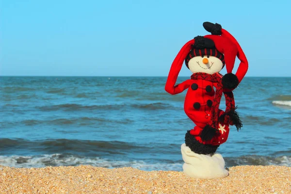 Christmas, Travel, Holidays Concept.Snowman In Red Clothes Standing On The Beach.Happy Snowman at Ocean Beach. Happy New Year and Merry Christmas Traveling Destinations, Tropical Vacations Concept.