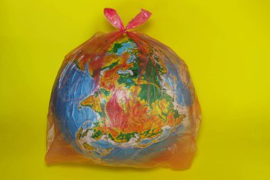 Arka plan. Dünya sarı arka plan üzerinde plastik torba. Çevre sorunları, doğa kirliliği ve ekoloji kavramı.