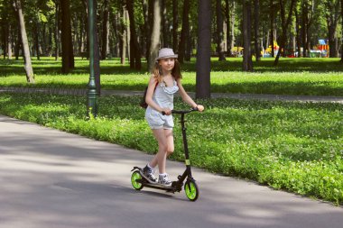 İnsanlar, çocuk, çocukluk kavramı. Genç kız açık havada yürüyüş. Sevimli kız parkta bir Scooter sürme. 