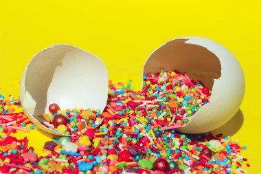 Sarı Arka Plan Üzerine Çok Renkli Şeker Tatlılar. Yumurta Kabuğu nda Çok Renkli Küçük Şekerler Closeup. Minimal Sanat Tasarımı. Tatlılar, Tatiller, Doğum Günü Konsepti. Kırık Yumurta ve Renkli Şekerler.