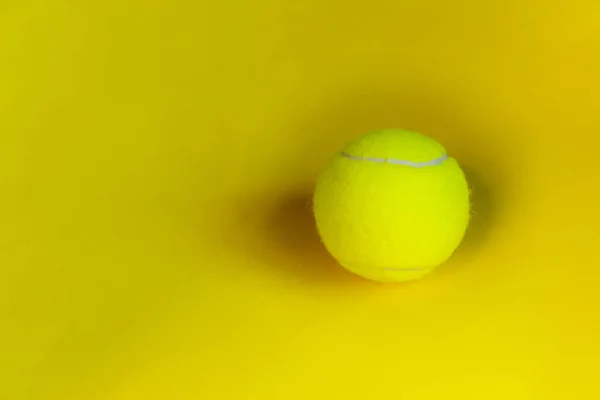 Yellow tennis ball over yellow background. Abstract sport background. Blurred yellow colors.