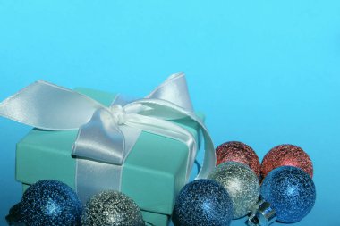 Mavi arka plan üzerinde Noel hediyesi ve süslemeleri. Tatiller, Noel oyuncakları konsepti. Mavi, kırmızı ve gümüş Noel topları ve mavi arka plan üzerinde yeşil hediye kutusu.