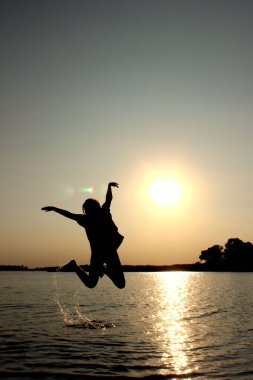 Dışarıda atlayan genç bir kız, günbatımı geçmişi. İnsanlar, seyahat, doğa konsepti.