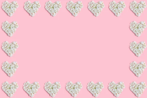 floral frame in pastel colors. hearts lined with white hydrangea flowers. pink background, flat lay, copy space.
