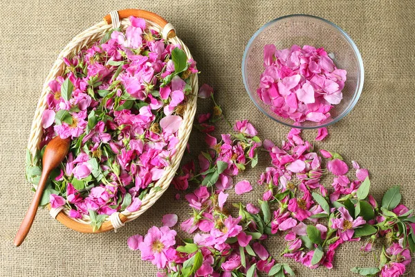 fragrant rose petals and flowers scattered on the background of canvas fabric. a glass bowl and a wicker basket with pink flowers. close-up, flat lay