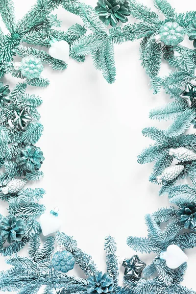 Holiday layout. beautiful frame made from branches of a fir tree and decorated with toys and pine cones on a white background. beautiful turquoise tinting. copy space, flat lay.