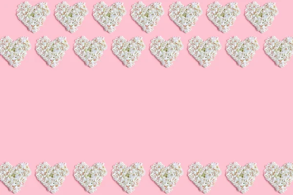 the floral concept in pastel colors. frame made hearts of white hydrangea flowers on a pink background. Valentine\'s day layout. space for text, top view.