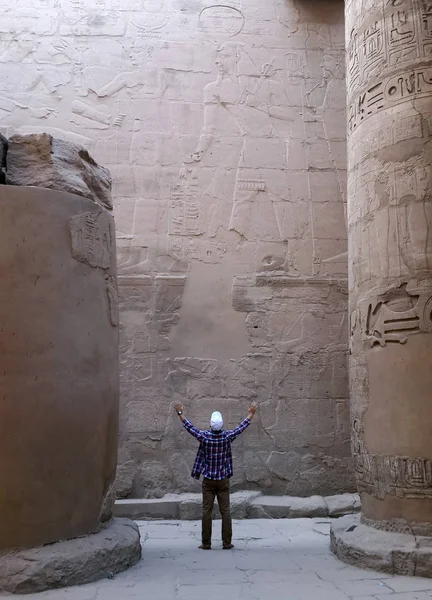 man standing with rises hands near ancient symbols of ancient Egypt on the wall