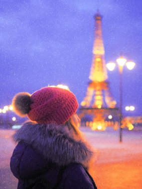 Geceleri Eyfel Kulesi 'nin yanındaki karlı Paris' te genç bir kadın.