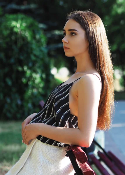 Chica joven modelo posando en el parque cerca de banco rojo —  Fotos de Stock