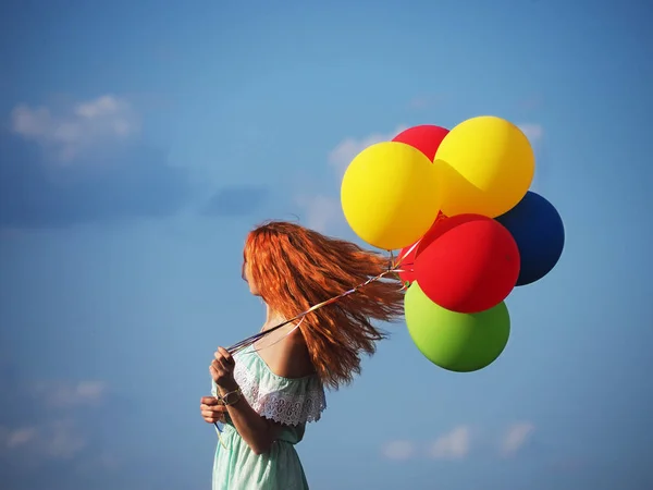 Mladý ryšavý dívka s barevnými balónky stojící na modré s — Stock fotografie