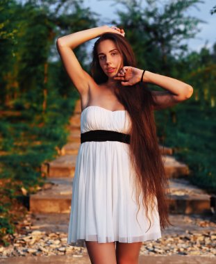 Beyaz elbiseli genç esmer manken merdivenlerde oturuyor.