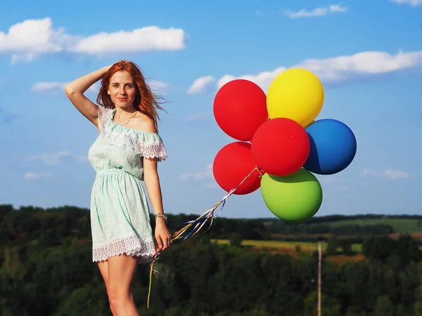 Jong roodharig meisje met kleurrijke ballonnen staan op de blauwe s — Stockfoto