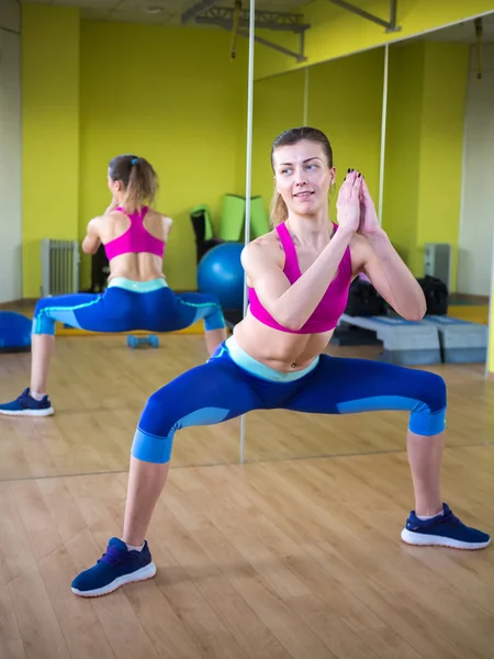 Chica modelo joven hace ejercicios en el gimnasio frente al espejo — Foto de Stock