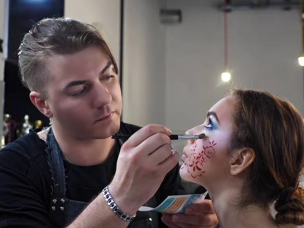 Make-up artist makes make-up at the young model and drawing a pi
