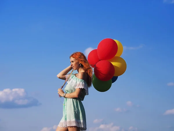 Mladý ryšavý dívka s barevnými balónky stojící na modré s — Stock fotografie