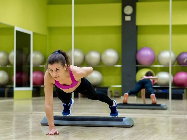 Chica modelo joven hace ejercicios en el gimnasio frente al espejo — Foto de Stock