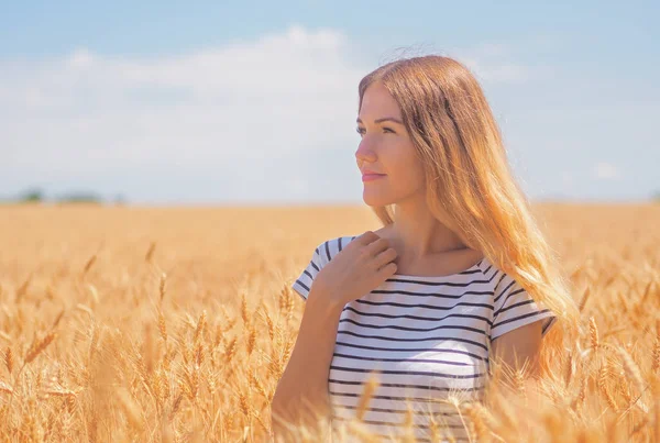 Mladá žena na pšeničném poli pod modrou oblohou za slunečného dne — Stock fotografie