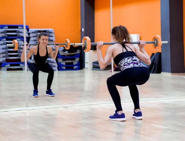 Jong model meisje maakt oefeningen in de sportschool in de voorkant van spiegel — Stockfoto