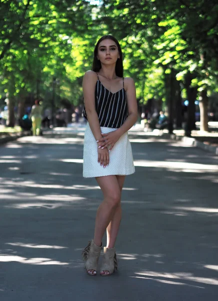 Chica joven modelo posando en el parque de pie y mirando vino —  Fotos de Stock