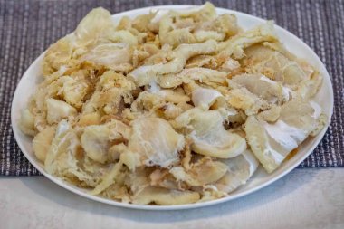 Tuzlanmış ve kurutulmuş, yuvarlak beyaz bir tabakta, gadus makrosefalus morina filetosu parçaları.