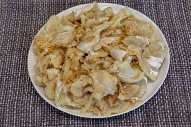 Tuzlanmış ve kurutulmuş, yuvarlak beyaz bir tabakta, gadus makrosefalus morina filetosu parçaları.