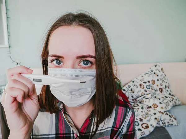 Mädchen in Krankenhausmaske mit Thermometer in der Hand Stockbild