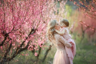 Küçük kızı ile genç güzel annesinin portresi. Yine de sevgi dolu aile, yakın. Çocuğunu pembe çiçekler içinde tutarak ve gülümseyen çekici kadın