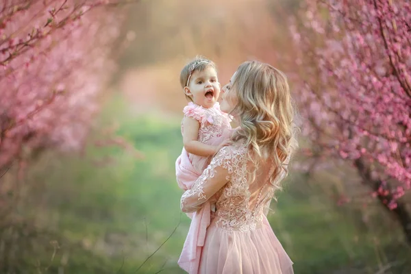 Retrato de la joven y hermosa madre con su pequeña niña. De cerca todavía de la familia cariñosa. Mujer atractiva sosteniendo a su hijo en flores rosadas y sonriendo —  Fotos de Stock
