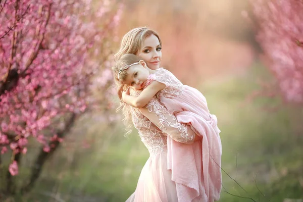 Portrait of young beautiful mother with her little girl. Close up still of loving family. Attractive woman holding her child in pink flowers and smiling — Stock Photo, Image