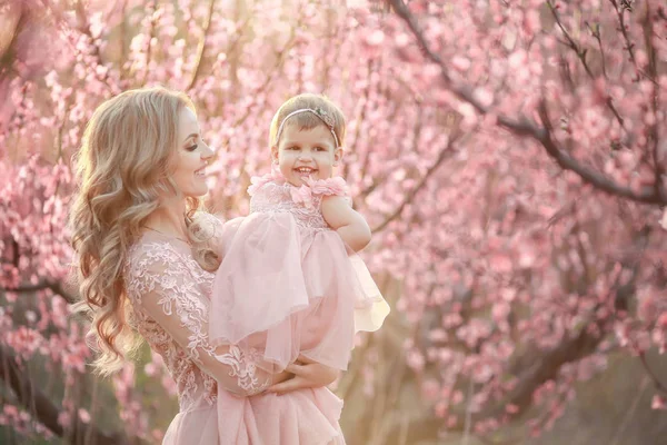 Portrait of young beautiful mother with her little girl. Close up still of loving family. Attractive woman holding her child in pink flowers and smiling — Stock Photo, Image
