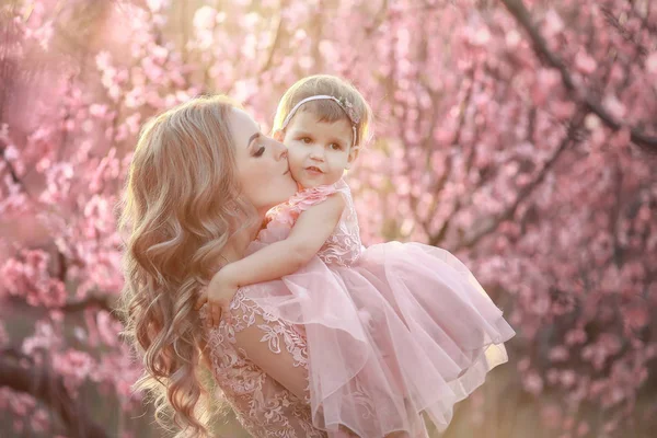 Retrato de la joven y hermosa madre con su pequeña niña. De cerca todavía de la familia cariñosa. Mujer atractiva sosteniendo a su hijo en flores rosadas y sonriendo —  Fotos de Stock