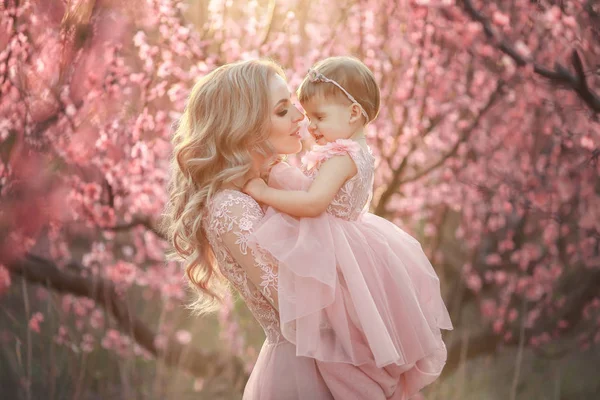 Portrait of young beautiful mother with her little girl. Close up still of loving family. Attractive woman holding her child in pink flowers and smiling — Stock Photo, Image